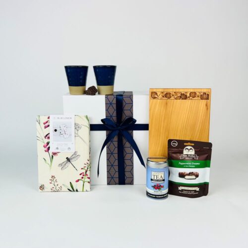 Kitchen Comforts Gift Hamper. A great new home gift basket. Including a stunning macrocarpa bread board, beautiful tea towel, two cups, herbal tea and a bag of Potter Brothers chocolates. Gifts for You & Me