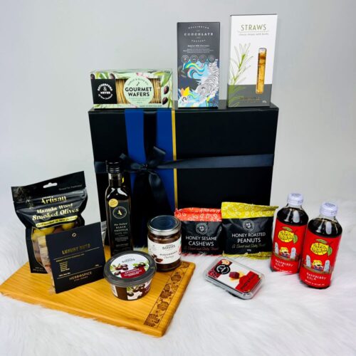 The Weekender Gift Box. Includes a Macrocarpa bread board, a bag of artisan olives, black truffle olive oil, luxury nuts, ploughmans chutney, honey roasted nuts, fruit paste, cheese & herb straws, honey sesame cashews, an antipasto, gourmet wafers, two bottles of Pete's Natural drinks and a bar of Wellington Chocolate Factory chocolate. A great corporate gift basket. Gifts for You & Me